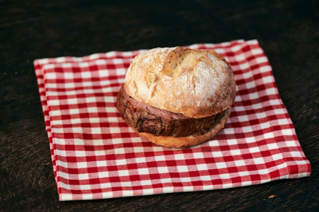 Ofenfrischer Leberkäse im knusprigen Brötchen auf rot-weißem Geschirrtuch serviert – klassische bayerische Brotzeit