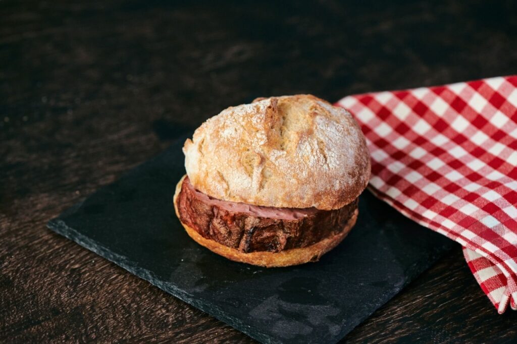 Rustikales Leberkäse-Brötchen mit knuspriger Kruste und hausgemachtem Leberkäse auf dunkler Schieferplatte
