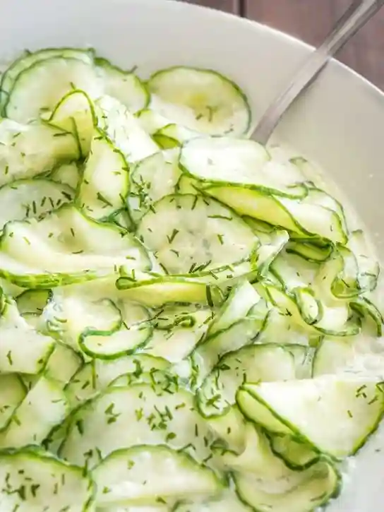 Nahaufnahme von Omas Gurkensalat mit Schmand und Dill in einer weißen Schale