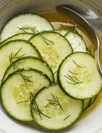 Nahaufnahme des Gurkensalat mit Dill auf einem weißen Teller, mit glänzenden Gurkenscheiben und feinem Dill, leicht im Essig-Dressing mariniert