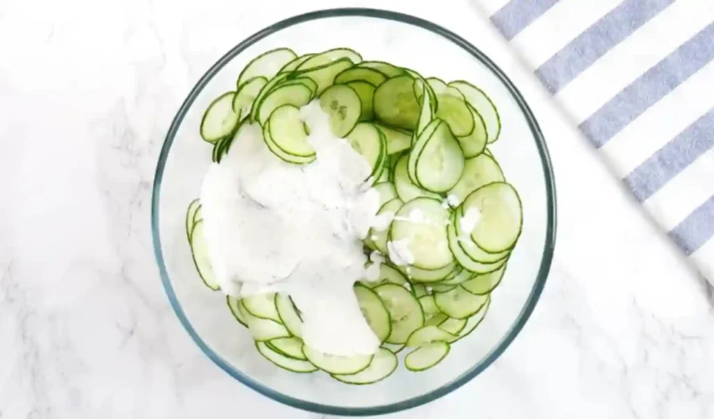 Gurkensalat Rezept mit Schmand-Dressing in einer Glasschüssel, bereit zum Vermengen