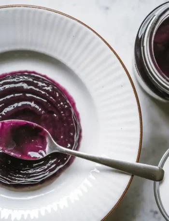 Zwetschgenmarmelade mit Lavendel auf einem Teller mit einer Marmeladenflasche und einem Löffel.