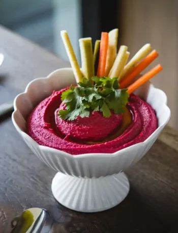 Rote Bete Hummus in einer modernen Schale auf einem stilvollen Tisch mit Gemüsesticks