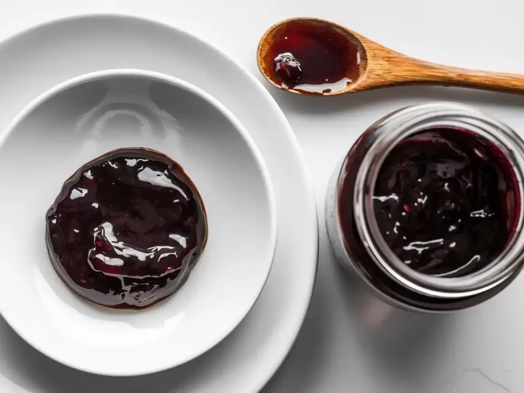 Zwetschgenmarmelade mit Rum auf einem modernen Teller, begleitet von einem Marmeladenglas und Holzlöffel.