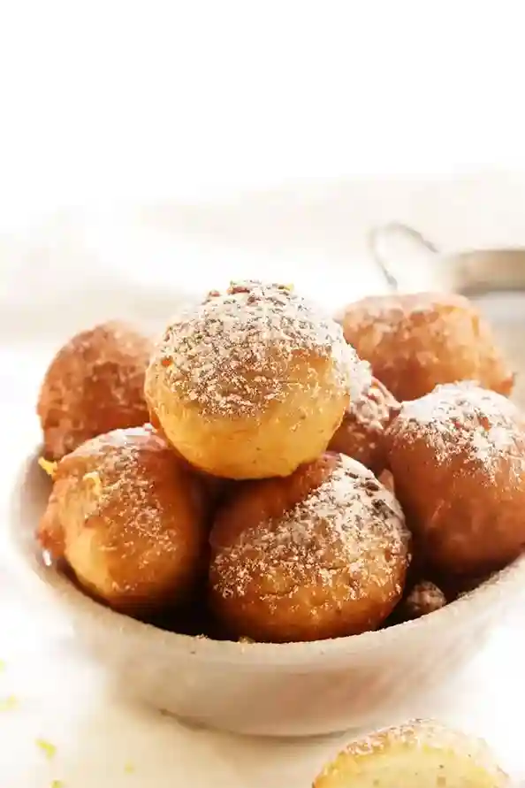 Frische Quarkbällchen nach Omas Rezept, goldbraun ausgebacken, mit feinem Puderzucker bestäubt und in einer weißen Schale serviert.