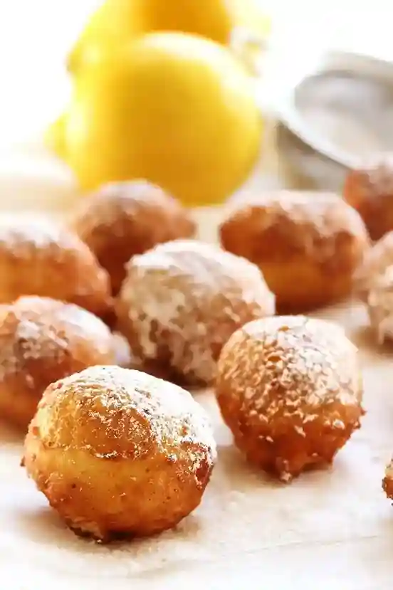 Frische Quarkbällchen nach Omas Rezept, goldbraun gebacken, mit Puderzucker bestäubt und mit Zitronen im Hintergrund.