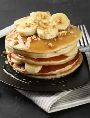 Stapel von fluffigen Bananen Pancakes ohne Ei, garniert mit frischen Bananenscheiben und Mandelsplittern.