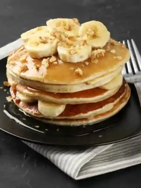 Stapel von fluffigen Bananen Pancakes ohne Ei, garniert mit frischen Bananenscheiben und Mandelsplittern.