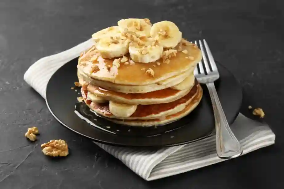 Stapel von fluffigen Bananen Pancakes ohne Ei, garniert mit frischen Bananenscheiben und Mandelsplittern.