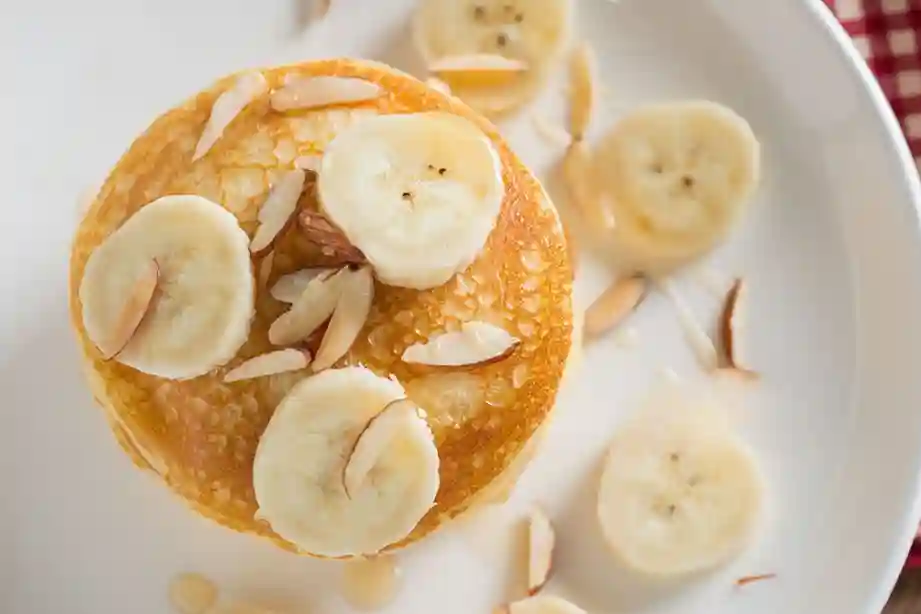 Nahaufnahme von Bananen Pancakes ohne Ei, reichlich belegt mit Bananenscheiben und Honig beträufelt.