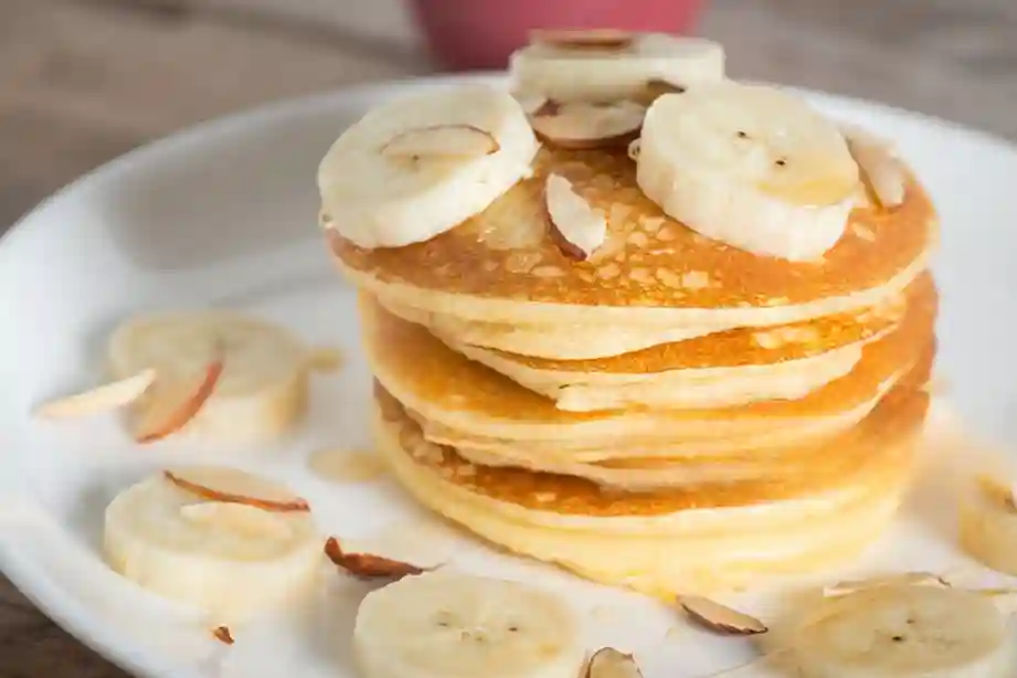 Appetitlich servierter Teller mit Bananen Pancakes ohne Ei, garniert mit Bananenscheiben und einem Guss aus Ahornsirup.