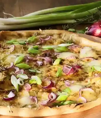 Frisch gebackener Flammkuchen vegetarisch mit roten Zwiebeln, Frühlingszwiebeln und Käse auf einem Holzbrett.