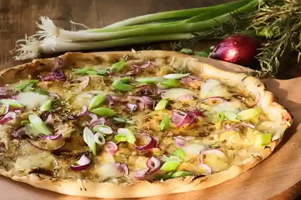 Frisch gebackener Flammkuchen vegetarisch mit roten Zwiebeln, Frühlingszwiebeln und Käse auf einem Holzbrett.