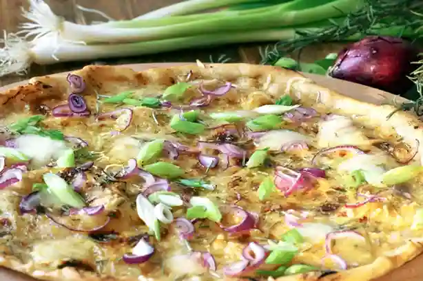 Knuspriger Flammkuchen vegetarisch mit Frühlingszwiebeln und roten Zwiebeln auf einem Holzbrett.