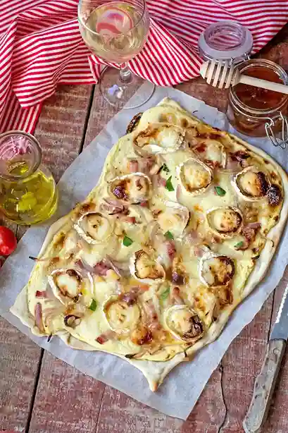 Flammkuchen vegetarisch mit Ziegenkäse, Zwiebeln und Honig auf knusprigem Teig, serviert auf rustikalem Holztisch.