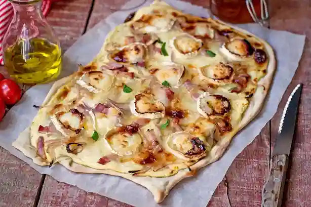 Flammkuchen vegetarisch mit knusprigem Teig, Ziegenkäse, roten Zwiebeln und Honig, serviert auf Backpapier.