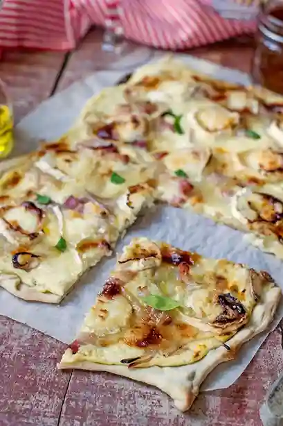 Flammkuchen vegetarisch mit knusprigem Teig, Ziegenkäse, roten Zwiebeln und Honig, frisch serviert auf Backpapier.