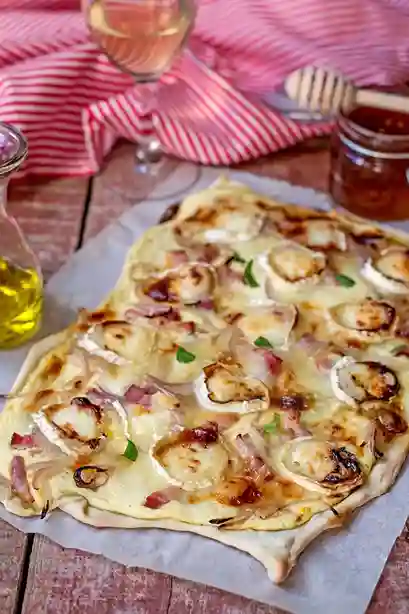 Flammkuchen vegetarisch mit Ziegenkäse, karamellisierten Zwiebeln und Honig auf knusprigem Teig, serviert auf rustikalem Holztisch.