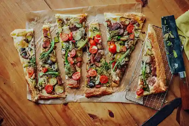 In Stücke geschnittener Flammkuchen Vegan mit frischem Gemüse auf Backpapier