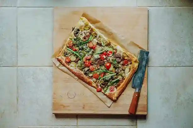 Frisch gebackener Flammkuchen Vegan auf einem Holzbrett mit rustikalem Messer