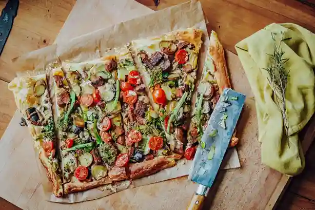 Frisch gebackener Flammkuchen Vegan mit buntem Gemüse und knusprigem Rand, geschnitten auf einem Holzbrett