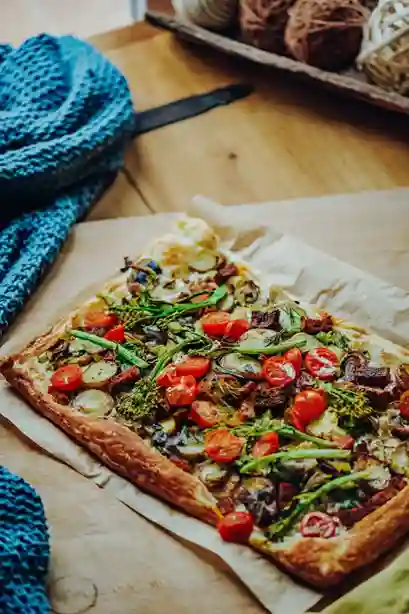 Flammkuchen Vegan mit buntem Gemüsebelag auf einem Holzbrett, knusprig gebacken und servierfertig.