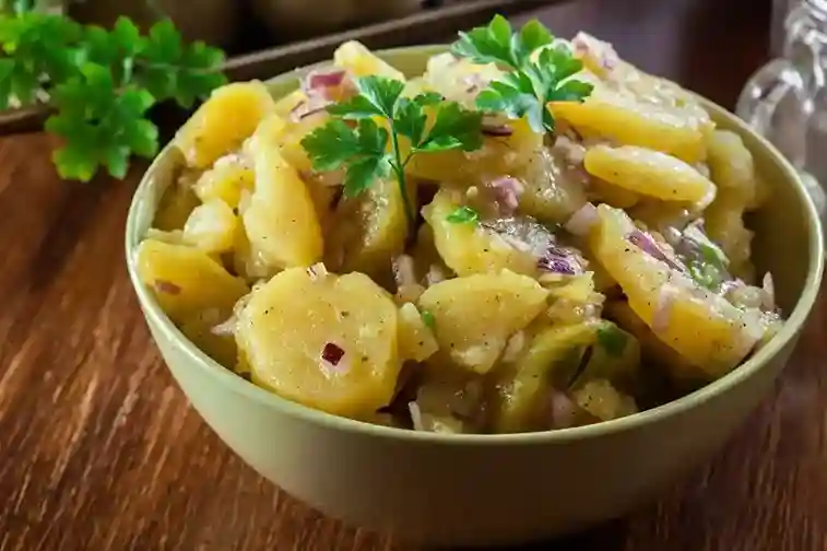 Ein authentischer DDR Kartoffelsalat ohne Mayonnaise in einer Schüssel, zubereitet mit Essig-Öl-Dressing, roten Zwiebeln und frischen Kräutern.