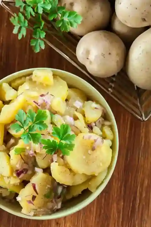 Eine Schüssel mit DDR Kartoffelsalat ohne Mayonnaise, verfeinert mit Essig-Öl-Dressing, roten Zwiebeln und frischen Kräutern – ein Klassiker der ostdeutschen Küche.