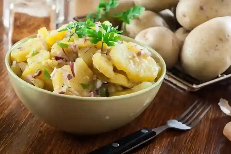 Eine Schüssel mit DDR Kartoffelsalat ohne Mayonnaise, zubereitet mit Essig-Öl-Dressing, roten Zwiebeln und frischen Kräutern – ein Klassiker aus der ostdeutschen Küche.