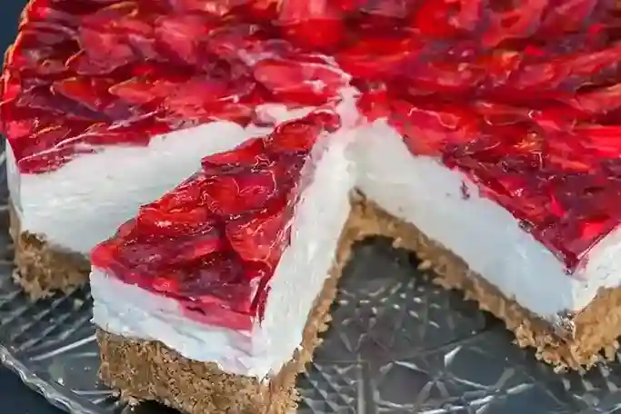 Ein angeschnittener Erdbeerkuchen ohne Backen mit Keksboden und Mascarpone, mit glänzendem Erdbeer-Topping und cremiger Mascarpone-Schicht, serviert auf einer Glasplatte.