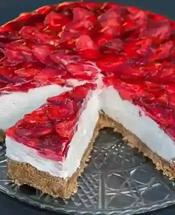 Ein köstlicher Erdbeerkuchen ohne Backen mit Keksboden und Mascarpone, verziert mit frischen Erdbeeren und rotem Tortenguss, auf einer eleganten Glasplatte serviert.