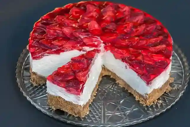 Ein köstlicher Erdbeerkuchen ohne Backen mit Keksboden und Mascarpone, verziert mit frischen Erdbeeren und rotem Tortenguss, auf einer eleganten Glasplatte serviert.