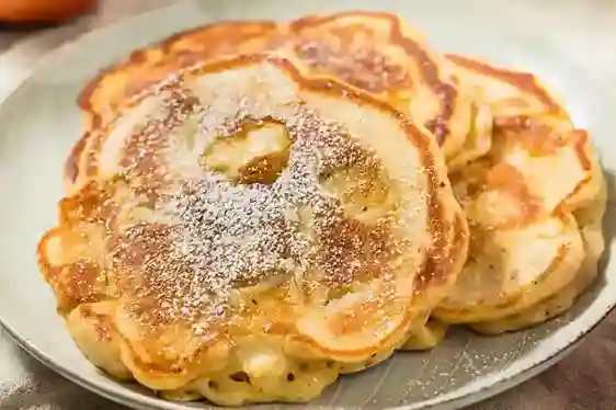 Goldbraun gebratene Apfelpfannkuchen mit Puderzucker bestreut auf einem Teller – ein klassisches Apfelpfannkuchen Rezept, perfekt für ein süßes Frühstück oder als Dessert.