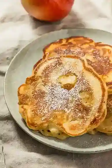 Frisch gebratene Apfelpfannkuchen auf einem Teller, mit Puderzucker bestreut – ein klassisches Apfelpfannkuchen Rezept, perfekt für Frühstück oder Dessert.