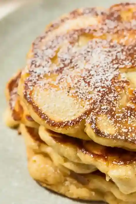 Nahaufnahme eines Stapels goldbrauner Apfelpfannkuchen mit Puderzucker – ein perfektes Apfelpfannkuchen Rezept für ein süßes Frühstück.