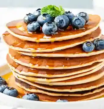 Ein Stapel fluffiger Pfannkuchen vegan einfach, garniert mit frischen Blaubeeren und Ahornsirup, serviert auf einem weißen Teller.