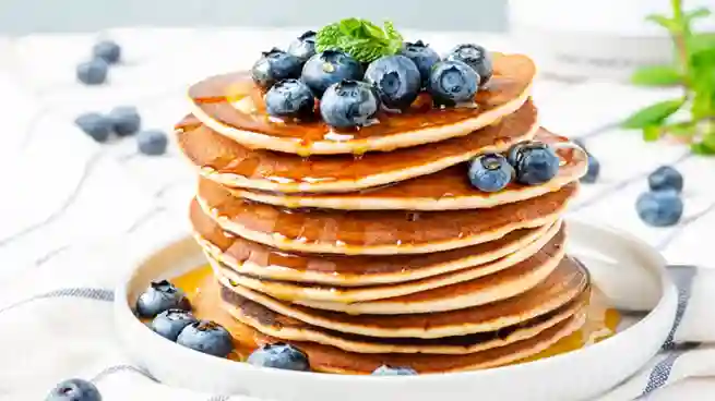 Ein Stapel fluffiger Pfannkuchen vegan einfach, garniert mit frischen Blaubeeren und Ahornsirup, serviert auf einem weißen Teller.