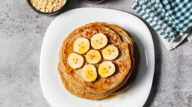 Ein Teller mit Haferflocken Bananen Pancakes, dekoriert mit frischen Bananenscheiben und einem Hauch Ahornsirup, von oben fotografiert.