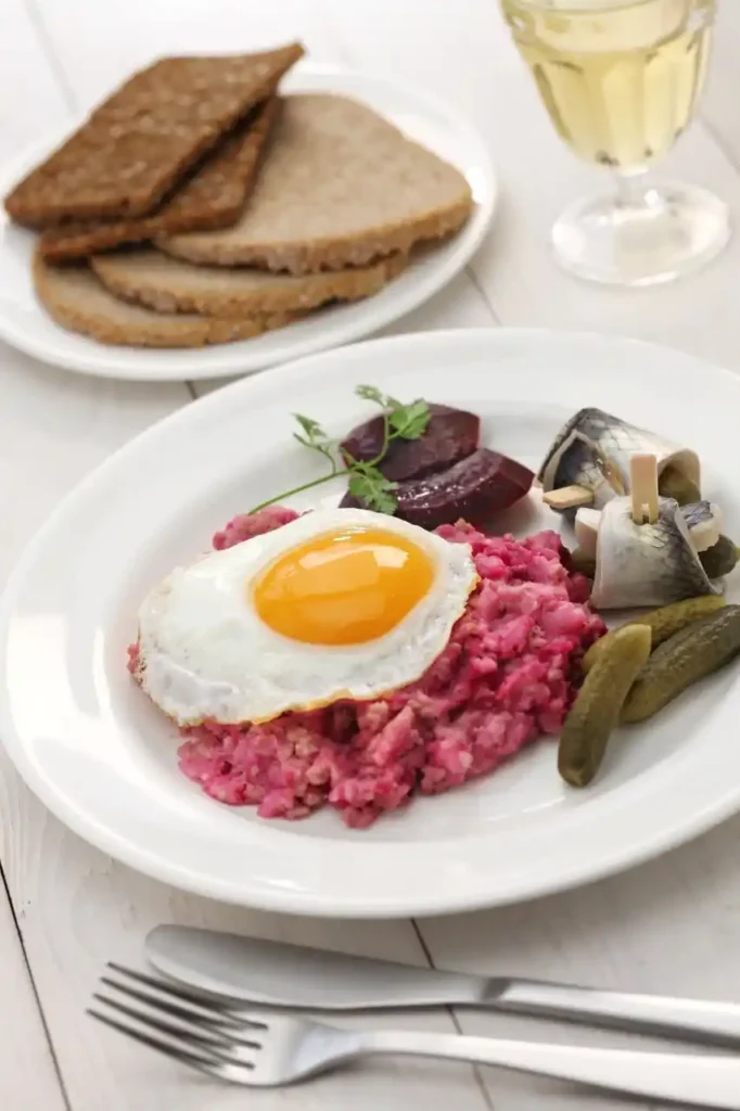 Labskaus Rezept – Norddeutsches Gericht mit Spiegelei, Gewürzgurken, Roter Bete, Rollmops und Brot, angerichtet auf einem Teller.