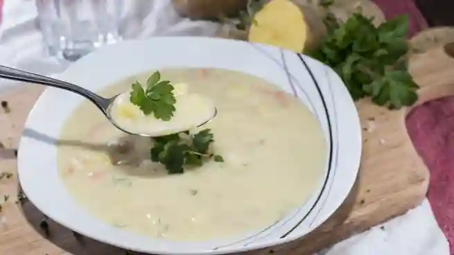 Ein Löffel cremige Kartoffelsuppe, garniert mit Petersilie, über einem Teller – ein leckeres Kartoffelsuppe Rezept vegetarisch.