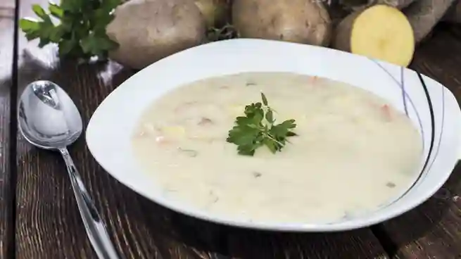 Ein Teller cremige Kartoffelsuppe mit Petersiliengarnitur auf einem rustikalen Holztisch – ein klassisches Kartoffelsuppe Rezept vegetarisch.