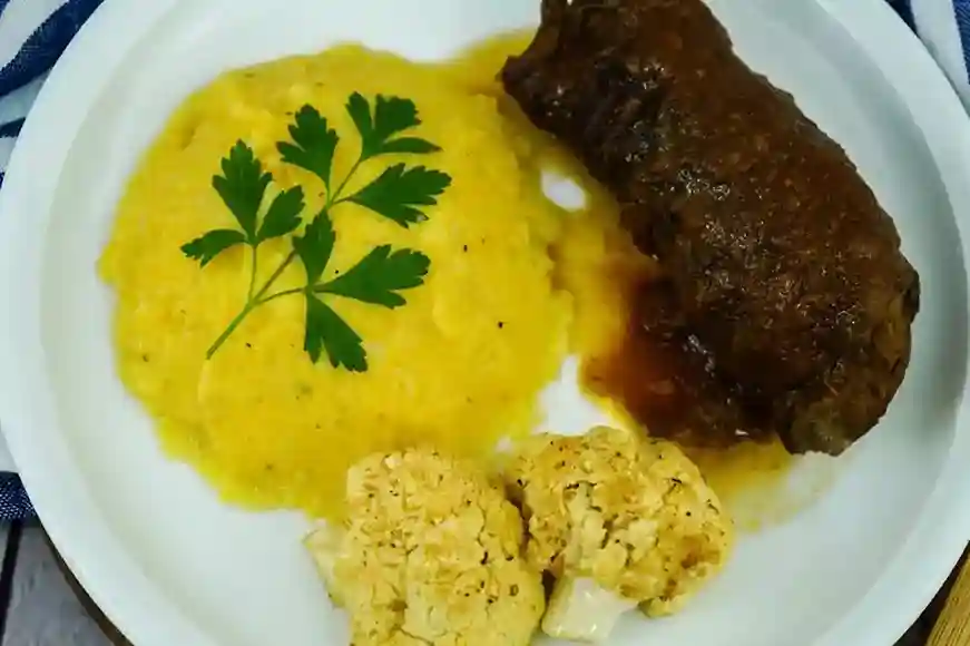 Rouladen im Schnellkochtopf mit cremigem Kartoffelpüree, geröstetem Blumenkohl und frischer Petersilie auf einem weißen Teller serviert.