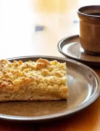 Ein Stück Streuselkuchen ohne Hefe auf einem braunen Teller, serviert mit einer Tasse Kaffee – perfekt für eine gemütliche Kaffeepause.