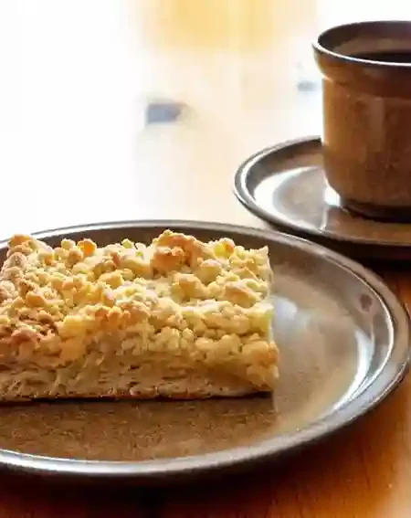 Ein Stück Streuselkuchen ohne Hefe auf einem braunen Teller, serviert mit einer Tasse Kaffee – perfekt für eine gemütliche Kaffeepause.