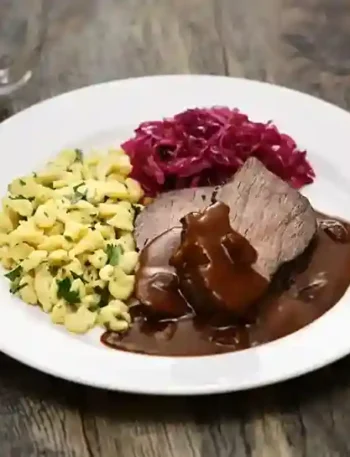 Ein traditioneller Teller mit fertig eingelegten sauerbraten zubereiten, serviert mit Spätzle, Rotkohl und einer aromatischen Soße – ein echter Genuss!