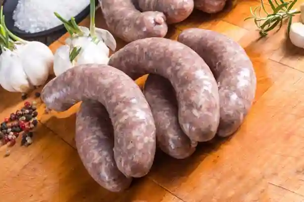 Frische grobe Bratwurst roh, auf einem Holzbrett mit Knoblauch, Pfefferkörnern und Rosmarin.