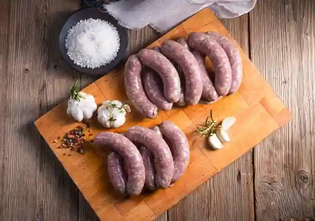 Frische grobe Bratwurst auf einem Holzbrett, umgeben von Knoblauch, Salz und Gewürzen – bereit für die Zubereitung.