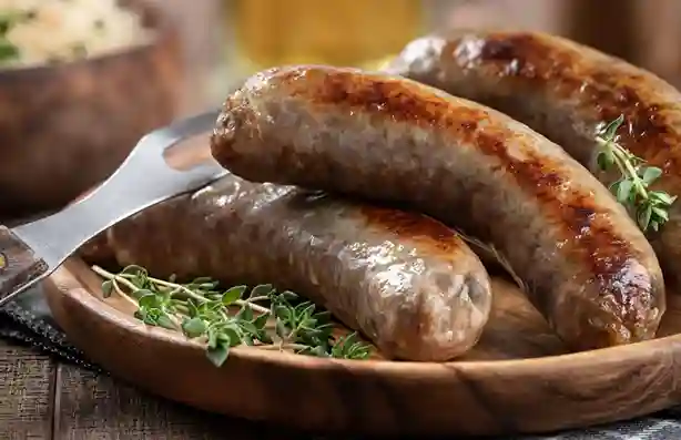 Grobe Bratwurst frisch gebraten, serviert auf einem rustikalen Holzteller mit Kräutern.