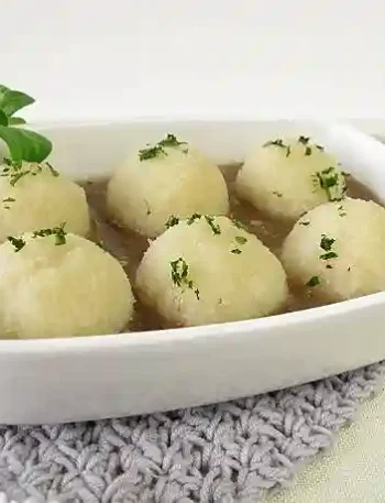 Kartoffelklöße Thermomix in einer weißen Auflaufform, serviert mit brauner Soße und frischer Petersilie