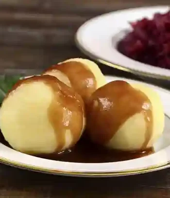 Drei Kartoffelklöße mit Sauce für Knödel auf einem Teller, serviert mit Rotkohl als Beilage.
